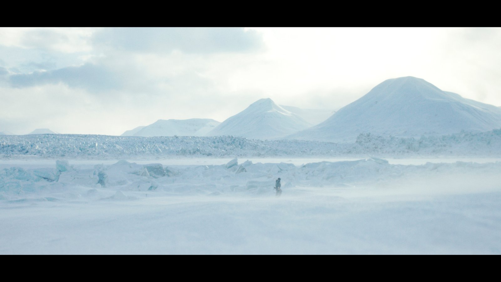 Plan large, un homme marche dans le blizzard face à un glacier