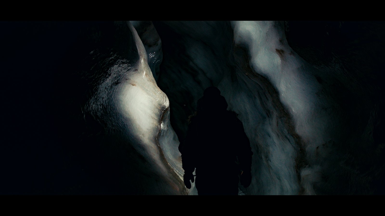 Plan large, un homme progresse dans une grotte de glace